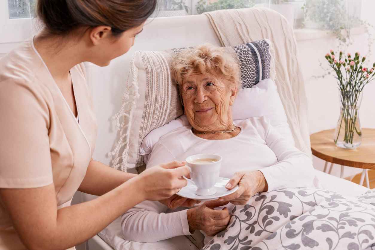 A private nurse serving tea to an elderly woman in her home.