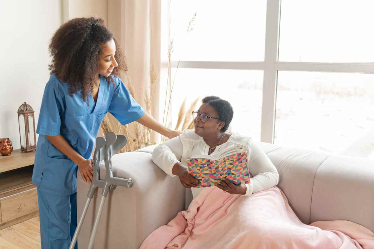 Lying on sofa. Aged woman with leg injury lying on sofa and talking to pleasant caring nurse