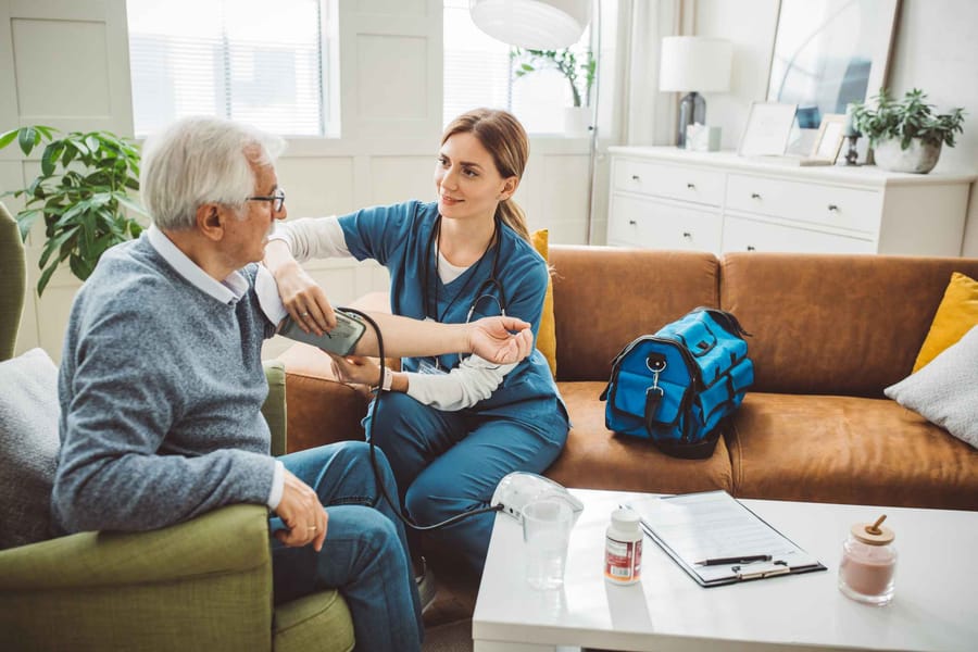 Nurse visiting mature patient at home. She is measuring his blood pressure in his living room.