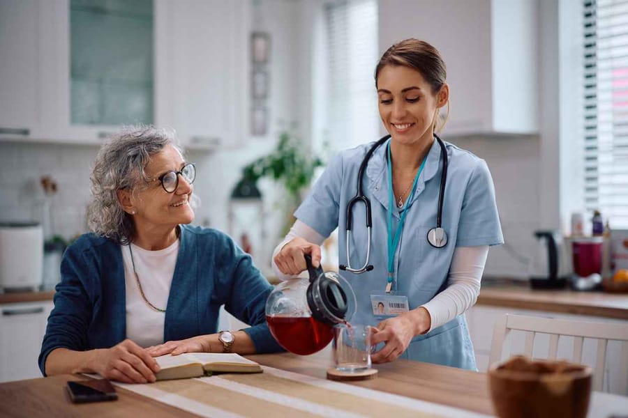 In-home nurse smiling as she pours a cup of coffee for her patient at home.