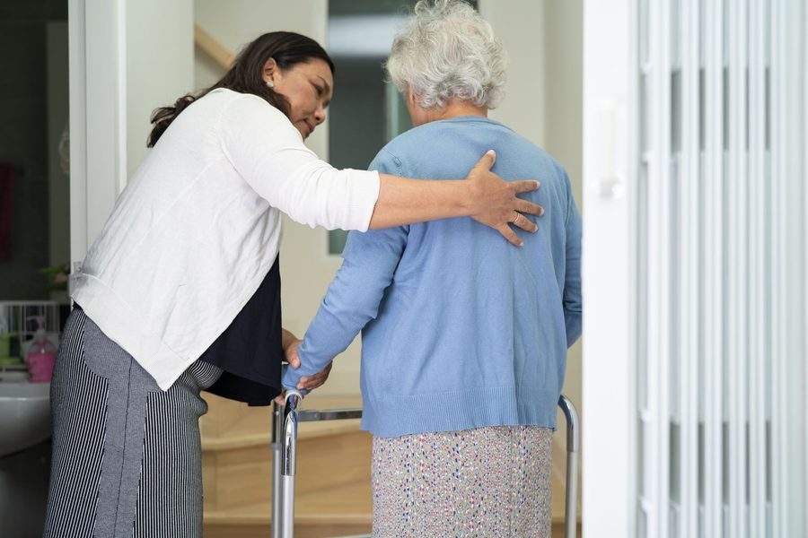 Caregiver assisting an elderly woman around the house with a walker to prevent falling